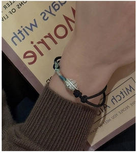 Detail of S925 silver tortoise shell pendant on black woven rope bracelet worn by model