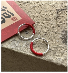 Macro detail of silver clip-on earrings with red thread wrap and lucky Fu card backdrop