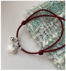 Detail of red braided cord bracelet with brushed silver heart charm and tweed fabric