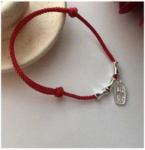 Close-up of red braided rope bracelet with silver bamboo beads and Zhaocai charm