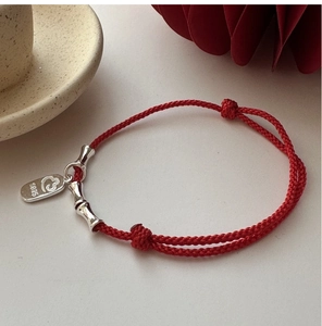Detail of red braided string bracelet with S925 silver bamboo tube and logo tag