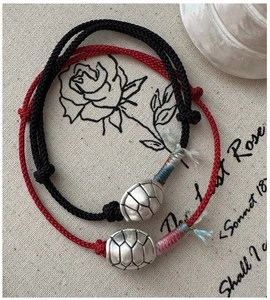 Detail of red and black woven bracelets with silver turtle shell charms on vintage fabric
