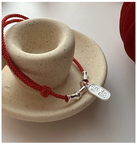 Detail of red braided bracelet with silver bamboo beads and wealth-themed pendant tag