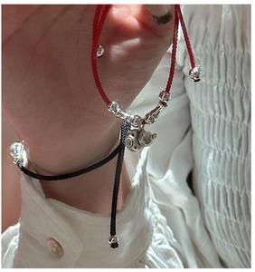 Gros plan de bracelets tressés rouges et noirs avec pendentif chat de fortune en argent