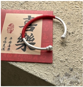 Détail d'un bracelet jonc argenté avec cordon rouge tressé et embouts ronds sur carte