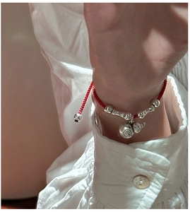 Détail du bracelet en corde rouge avec cloche de fortune en argent et pendentif cacahuète