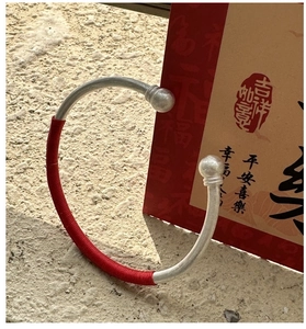 Détail d'un jonc en argent avec tissage de fil rouge et perles sur carte festive