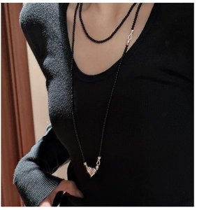 Detail of long black bead necklace with silver heart pendant worn on black knit sweater