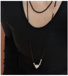 Detail of a black onyx bead necklace with a heart-shaped silver pendant on a black sweater