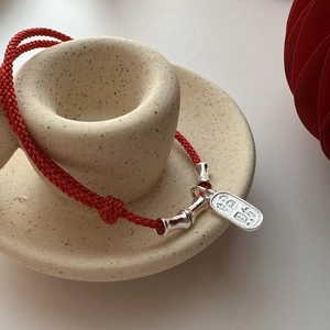 Red cord woven bracelet with silver bamboo tubes and lucky charm on ceramic stand