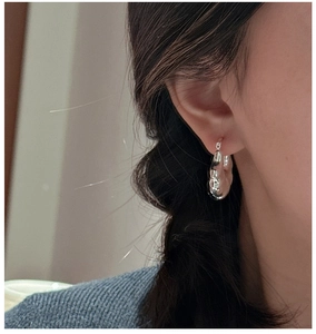 Detail view of silver hollow hoop earrings with irregular organic texture on a model