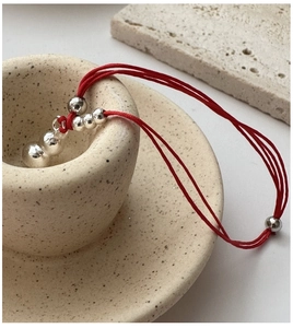 Close-up of red braided rope bracelet with polished silver beads on ceramic background
