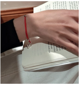 Detail of red string bracelet with silver beads on a person's wrist against a book