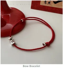 Detail eines roten geflochtenen Armbands mit silbernem Schleifenanhänger und Perlen