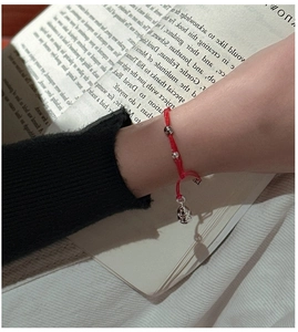 Close-up of handmade red braided bracelet with silver beads and gourd charm on wrist