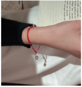 Minimalist red string bracelet with silver beads and small bell charm worn on wrist