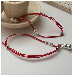 Close-up of red string bracelet with silver gourd charm and metal beads on stone base