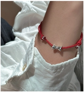 Nahaufnahme eines roten geflochtenen Armbands mit silbernem Schleifenanhänger am Handgelenk