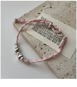 Détail d'un bracelet tissé rose et blanc avec perle nœud argentée sur texture pierre