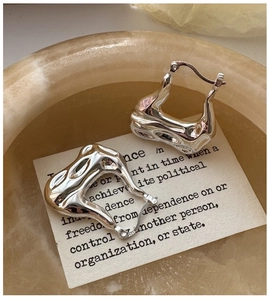 Close-up of irregular lava texture silver earrings placed in a stone bowl on a white card