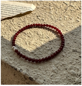 Detail of red agate beaded bracelet with silver charm on natural stone surface