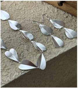 Detail shot of matte S925 sterling silver heart earrings and necklace on stone background