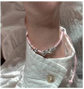 Vue détaillée du bracelet en corde tressée rose avec breloque nœud argenté au poignet