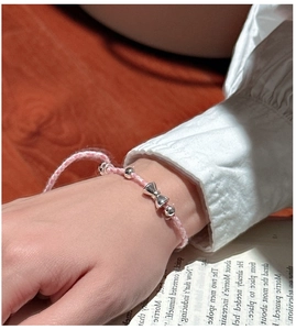 Gros plan d'un bracelet en corde tressée rose avec un pendentif nœud poli et des perles