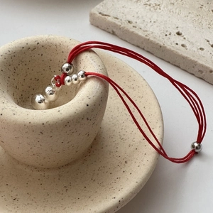 Traditional red woven cord bracelet with polished silver beads in a minimalist Zen setting