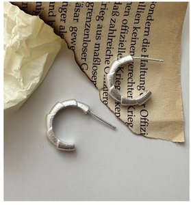 Macro detail of S925 silver C-shape earrings with matte texture and segmented design