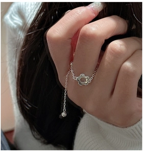 Gros plan d'une bague chaîne fleur en argent S925 portée au doigt avec un pull doux