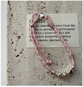 Gros plan d'un bracelet tressé rose et blanc avec charm nœud en argent S925 et fermoir mousqueton