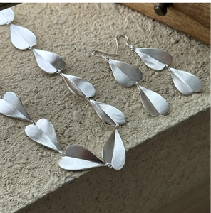 Detailed view of matte S925 silver leaf earrings and necklace set on stone background