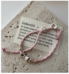 Détail du bracelet en corde tressée rose et blanc avec breloque nœud en argent et perles