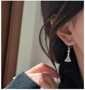 Detailed view of silver bell-shaped earrings with textured matte finish on a female model