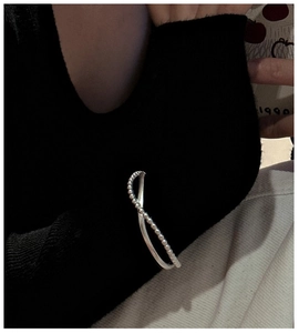 Detail of silver S925 cross wrap bangle with beads worn over a black knitted sleeve
