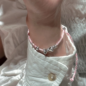 Bracelet tressé rose et blanc fait main avec pendentif nœud argenté sur le poignet