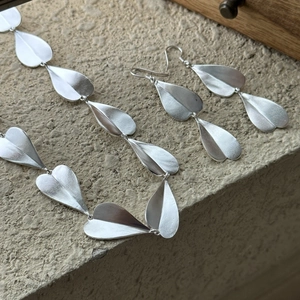 Matte S925 silver heart earring and necklace set displayed on a natural stone surface