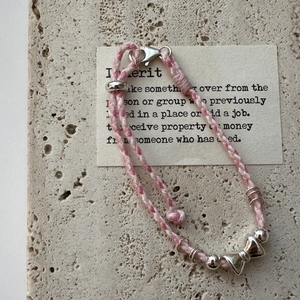 Bracelet en corde rose tissée argent S925 avec breloque nœud sur fond en travertin