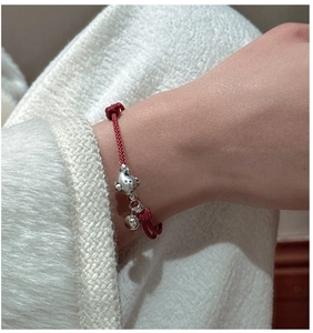 Détail macro d'un bracelet en corde tressée rouge avec un charme cochon en argent et grelot