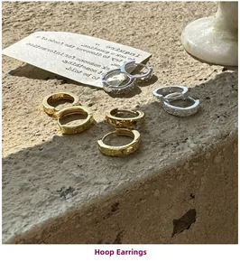 Gros plan de boucles d'oreilles créoles en argent et or martelé sur fond de pierre