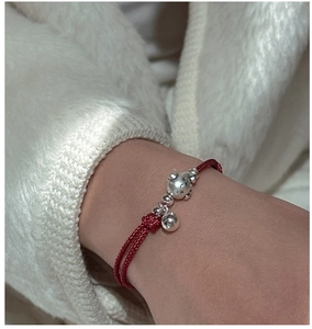 Détail d'un bracelet en corde tressée rouge avec breloque cochon argentée et cloche