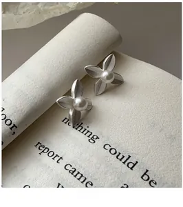 Detail of matte silver flower earrings with brushed texture and central white pearl accent