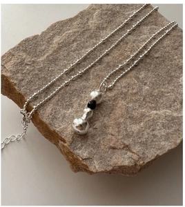 Détail d'un collier en argent S925 avec trois billes en pendentif posé sur une pierre