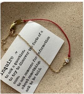 Detail of red braided string and gold chain bracelet with a sparkling round zircon charm