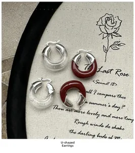 Détail de boucles d'oreilles en résine en U transparentes et bordeaux sur tissu vintage