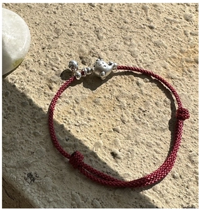 Détail du bracelet en cordon rouge tressé avec pendentif dauphin argenté et grelot