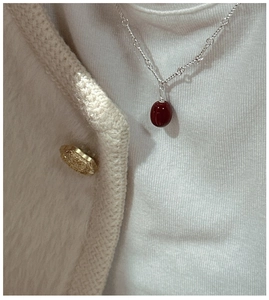 Detailed view of an S925 silver necklace featuring a deep red oval bean pendant on a model