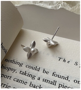 Macro view of matte silver flower earrings with pearls on a vintage book page background