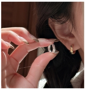 Vue macro de mini créoles martelées en argent et or tenues entre les doigts du mannequin